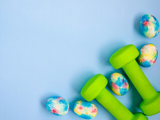 green heavy dumbbells, colorful easter eggs on blue background. Easter fitness and training frame composition with copy space. Top view from above, flat lay.