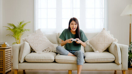 Beautiful young asian woman sitting on sofa and holding joystick playing online video game in living room at house