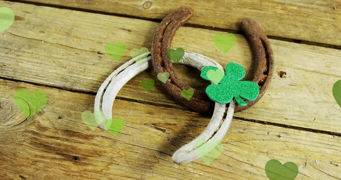 Animation of st patrick's shamrock, horseshoe and green hearts on wooden background