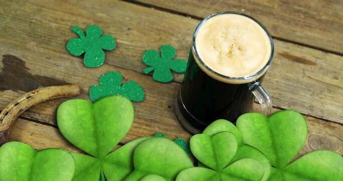 Animation of st patrick's day shamrock and glass of beer on wooden background