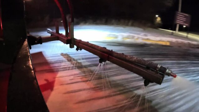 De-ice truck spraying de-ice fluid on public parking lot road during winter