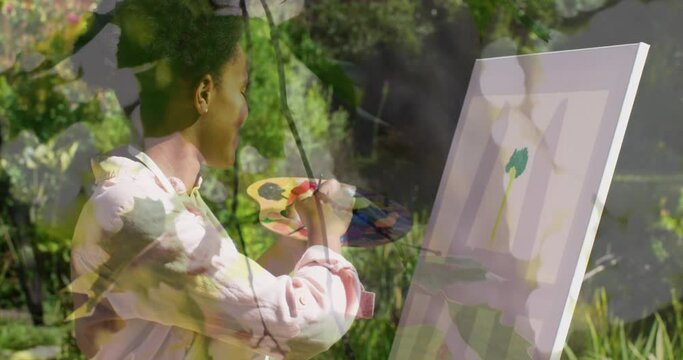 Animation of tree over african american woman painting on easel in garden