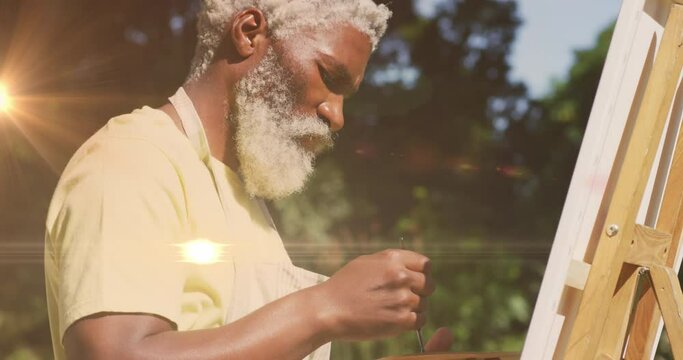 Animation of light trails over senior african american man painting on easel in garden