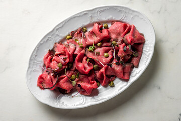 Sliced roast beef on white plate on white marble table top view