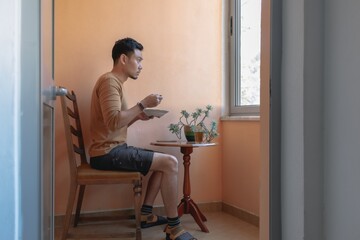 Asian man having breakfast soup on the terrace by the windows.