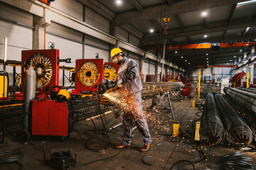 A metallurgy worker is grinding metal framework in facility.