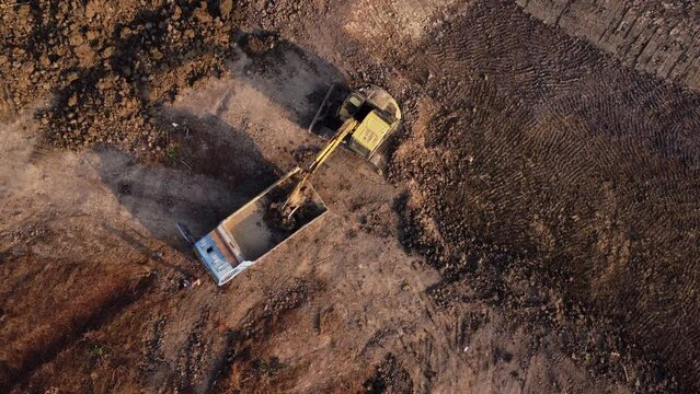 Aerial view of a wheel loader excavator with a backhoe loading sand onto a heavy earthmover at a construction site.