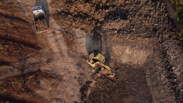 Aerial view of a wheel loader excavator with a backhoe loading sand onto a heavy earthmover at a construction site.