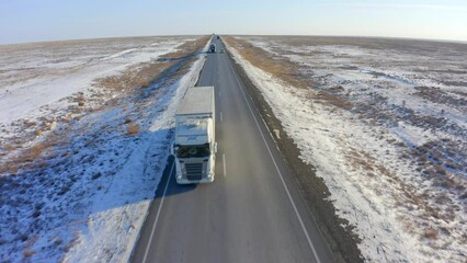 Front view of two trucks driving along the road in the endless steppe covered with snow
