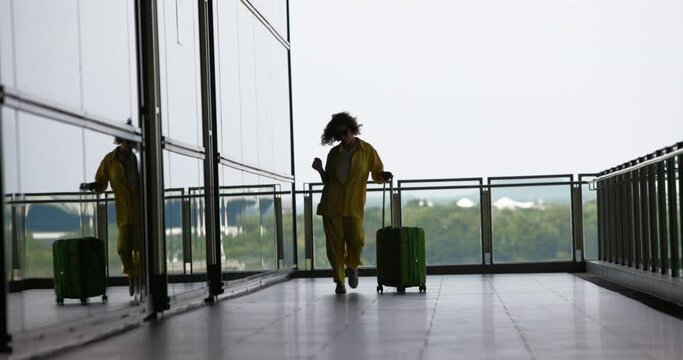 Silhouette of woman with luggage dancing happily, joyfully after arriving to another city. Woman came to city to her parents and happy to see them after long time. Woman joyfully dancing at airport