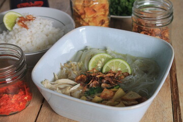 Indonesian food called soto ayam served on a blue bowl complete with rice, chili sauce, fried potato, lime  and fried onions
