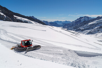 Fototapeta na wymiar An enormous red snow plow moves along the glacial surface at Jungfraujoch