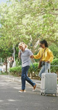 Vertical video of happy diverse couple walking with luggage in city