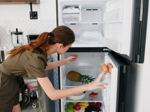 A woman opened the refrigerator and looks sadly into it, wondering what to cook, defrosted the refrigerator, freezer repair in the kitchen at home