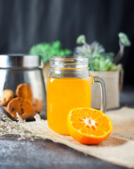 Fresh orange juice with fruit and green leaves and plants, on dark background