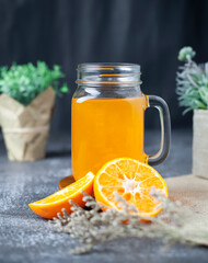 Fresh orange juice with fruit and green leaves and plants, on dark background