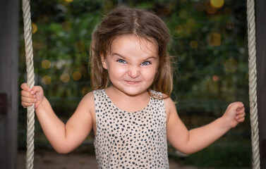 Portrait of a child girl with grimacing on a swing