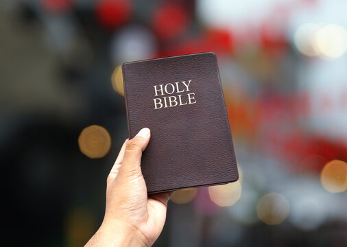 hand holding the holy bible book of chistianity. symbolic posture of prayer and worship. on bokeh background.