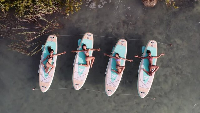 Four women hold a lower back stretch on stand up paddle boards during a yoga session on Bacalar Lake.