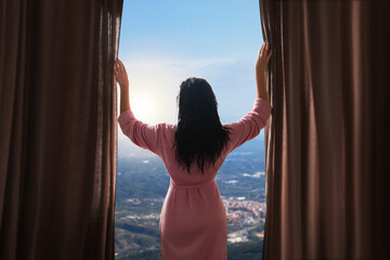 The girl from the back opens the curtains. Girl in a bathrobe. View from the window to the mountains
