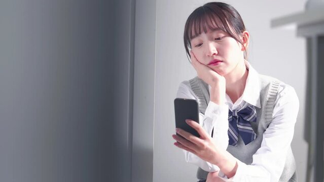 スマホを持って教室で落ち込む女子高生