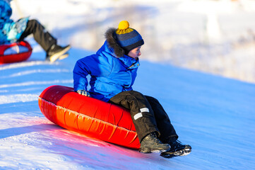 A little boy-child rides a tubing down a hill in the snow in winter. Winter entertainment. Snow...