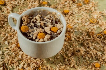 Dry chamomile flowers- tea time. Cup on yellow floral background