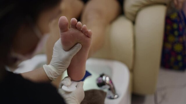Slow motion close up shot of a pedicure expert hands filing a client left foot in a nail salon