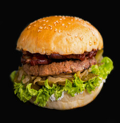Close-up of a delicious fresh homemade burger with lettuce, cheese, onion and tomato on a rustic wooden board on a dark background