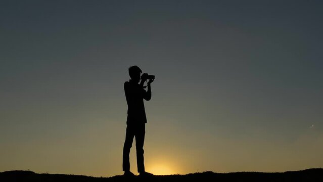 Silhouette of photograher with camera taking pictures at sunset sky, zoom in
