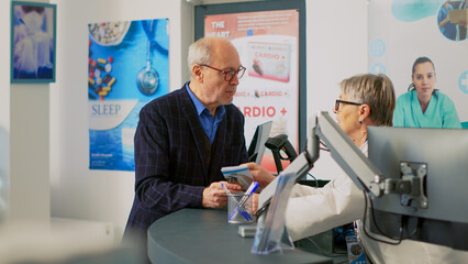 Obraz premium Senior adult talking to pharmacist at cash register counter, using medical leaflet to ask about healthcare treatment. Customer standing at pharmacy desk before buying products.