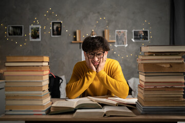 Student studying hard exam with books, tired guy read difficult book in dormitory. - obrazy, fototapety, plakaty