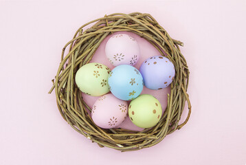 Painted multicolored eggs in wooden nest of branches on pink background. View from above. Easter, birth. Copy space