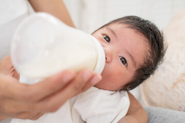 mother feeding baby boy with fresh milk in plastic bottle in bed closeup. mother breastfeeding and hugging baby. Young mom breast feeding her newborn child. Lactation infant concept.