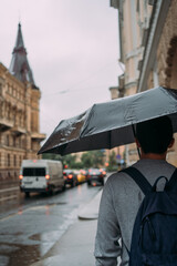 a man in a gray hoodie under a black umbrella in the city during the rain