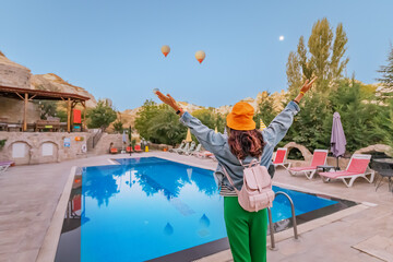 Girl admiring view of a flying hot air balloons with swimming pool with reflections