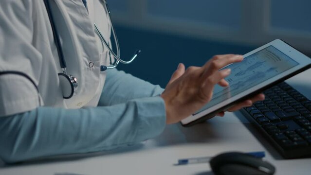 Close up of general practitioner holding tablet computer analyzing radiography while working over hours at medical expertise in hospital office. Doctor planning medication treatment for patient