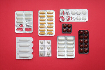 Pattern of random tablets and capsules pill in blister packaging on the red background. Pharmaceutical, antibiotic concept