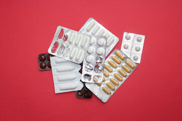 Random tablets and capsules pill in blister packaging on the red background. Pharmaceutical, antibiotic concept
