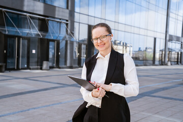 Portrait of successful business woman in stylish suit using laptop posing next to city office building. Confident female CEO smiling. Successful Diverse Business Manager.