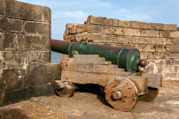 Fototapeta na wymiar A bronze cannon made at Barcelona in Spain located at the former fortress at Essaouira in Morocco. It faces towards the Atlantic Ocean. The cannon sits on a wooden gun carriage with wooden wheels.