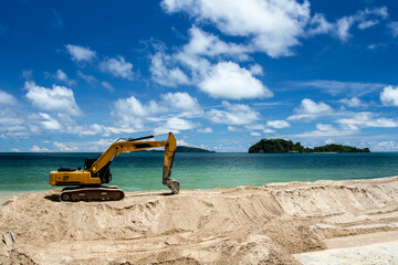 Excavator is scooping up sand on the beach with sky, sea and island background..Excavator is digging sand on the beach.