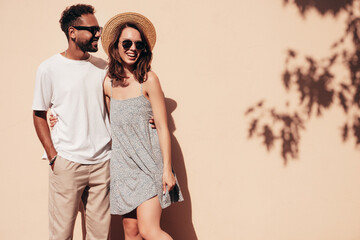 Smiling beautiful woman and her handsome boyfriend. Woman in casual summer clothes. Happy cheerful family. Female having fun. Sexy couple posing in the street near wall, at sunny day. In sunglasses