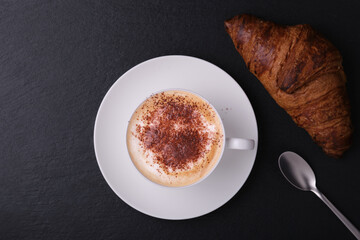 White cup with cappuccino on a dark background flat lay. Italian breakfast on a black background....