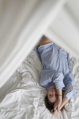 Portrait og beautiful natural looking brunette woman in blue cotton pajama shirt laying on the bed