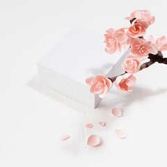 Valentine's Day stage mockup - white square podium, twig of gentle sakura flowers, petals in sunlight on white wood table, top view, japan style for presentation cosmetic products, goods, square.