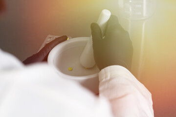 close shot of medical scientist grinding orange pills in mortar and pestle. Pharmacist