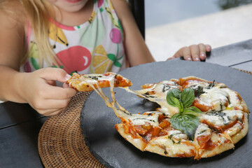 Little girl eating pizza Margherita at the restaurant
