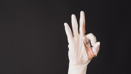 Ok hand sign and wear latex glove on black background.