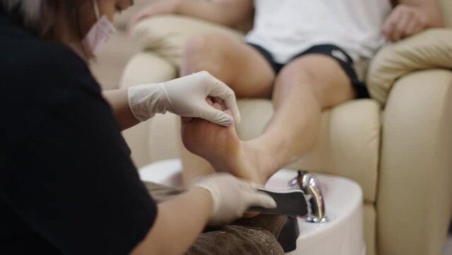 Close up of hands removing dead skin on man foot - Pedicure